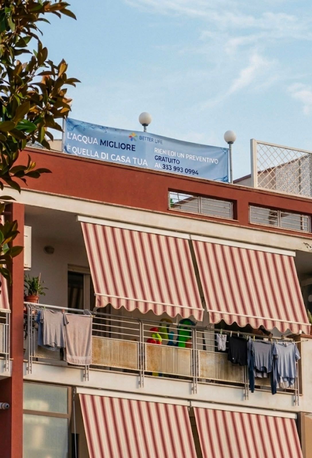 Banner BetterLife su una facciata residenziale con balconi e tende da sole